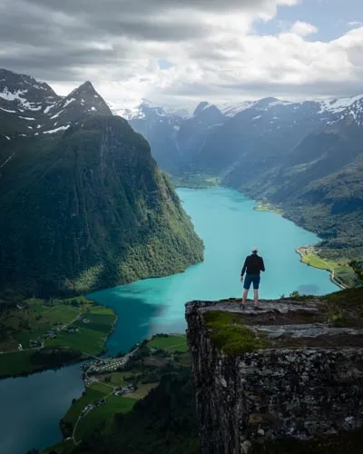 A hiker standing at the summit of Klovane, gazing out at the turquoise waters of Lake Oldevatnet, surrounded by mountains and glaciers in the Olden region of Norway.