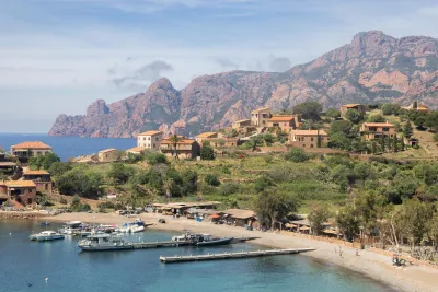 The village of Girolata as seen from the bay, with its colorful waterfront houses and the distinctive red cliffs of the Scandola Nature Reserve in the background.